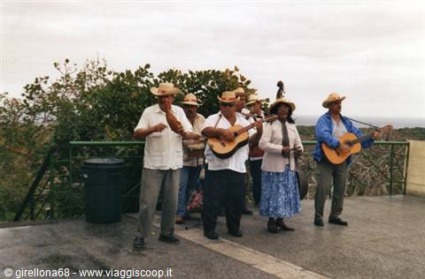 Musicians in straw hats playing guitars and maracas on a seaside terrace