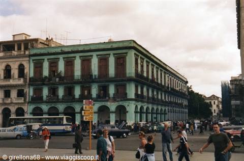Green colonial building with balconies, vintage cars and pedestrians, Havana