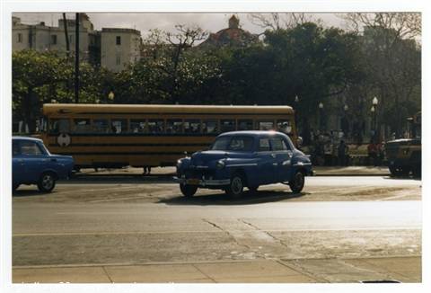 Vintage blue car and yellow bus cross a sunny city intersection