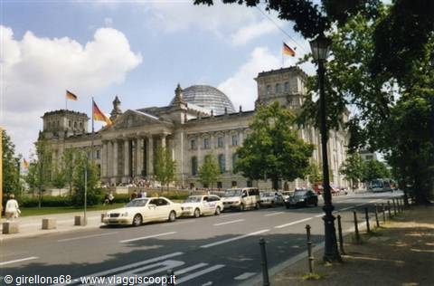 The Reichstag in Berlin with German flags and traffic under a cloudy sky