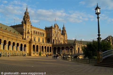 Tourists walk along the brick arcades of Plaza de España, Seville