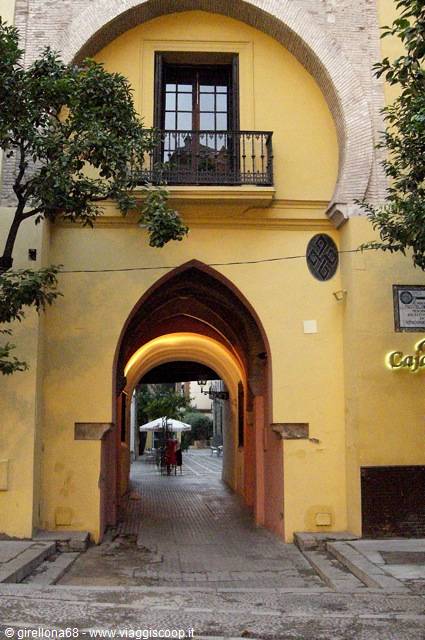 Horseshoe arch on yellow facade, wrought-iron balcony, shaded café beyond