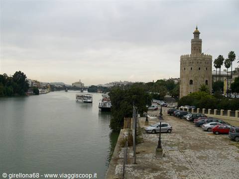 The Torre del Oro golden tower stands by the Guadalquivir with boats and parked cars