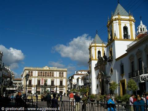 Tourists in the square by the white and yellow church with bell towers in Ronda