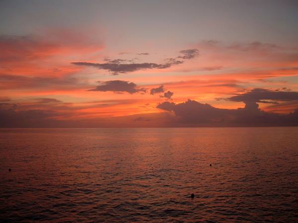 Red and orange sky over calm sea, dark clouds on the horizon