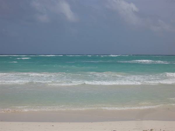 Turquoise waves breaking on a white sand beach, cloudy sky