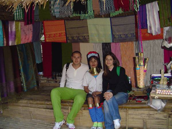 Tourists with long-neck woman beside colorful hanging textiles, Long Neck Village