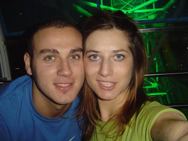 Young man and woman smile in selfie behind green-lit metal structure