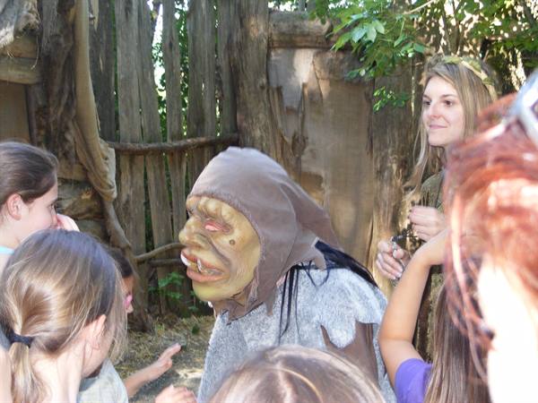 Actor in an ogre mask entertains children among wooden fences