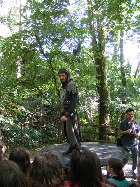 Actor in medieval costume on wooden stage among trees, performing for children