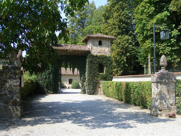 Ivy-covered stone gatehouse with gravel drive between hedges and trees