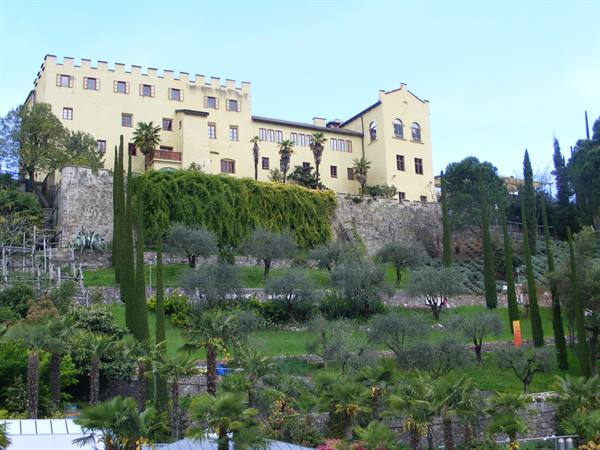 Yellow crenellated castle on a hill of olive trees and cypresses, Merano