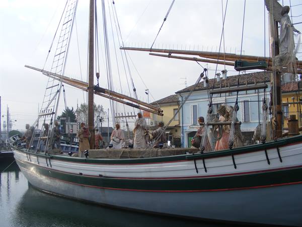 White and green sailing ship moored at the harbor with costumed figures aboard