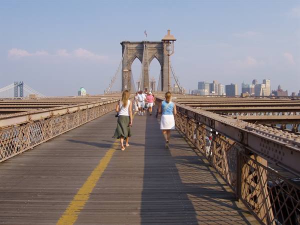 Tourists walk along the Brooklyn Bridge wooden walkway toward Manhattan skyline