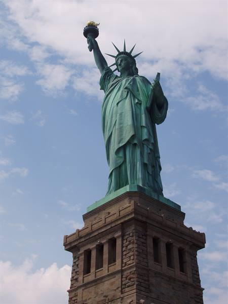 The verdigris copper Statue of Liberty raises her torch against a cloudy sky