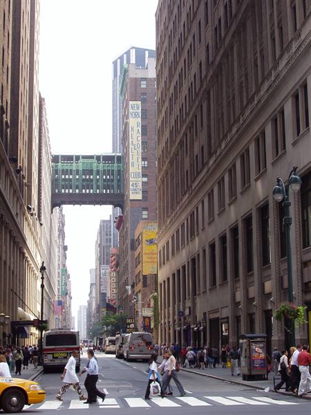 Pedestrians crossing a New York street between skyscrapers in bright morning light