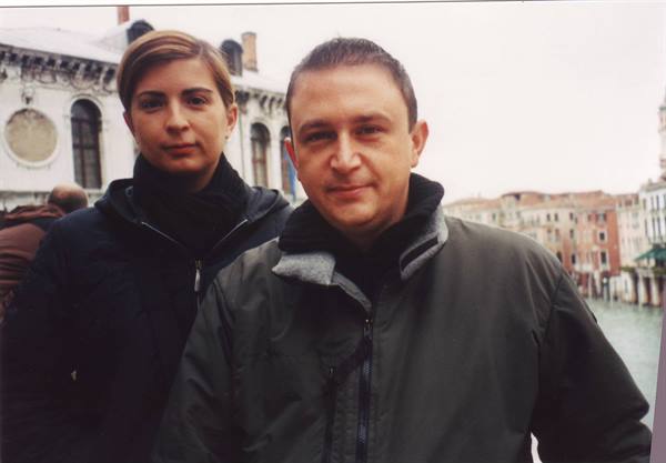 Couple in jackets on a bridge in Venice, buildings and canal behind