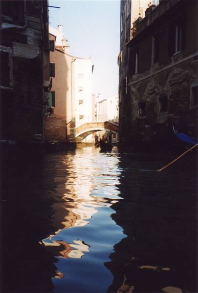 Venice canal, gondola passing under a bridge between old buildings, water reflections