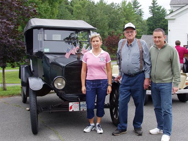 Three people beside a vintage black car with small American flags