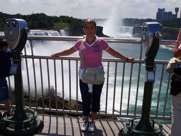 Woman in pink shirt between two coin binoculars in front of Niagara Falls