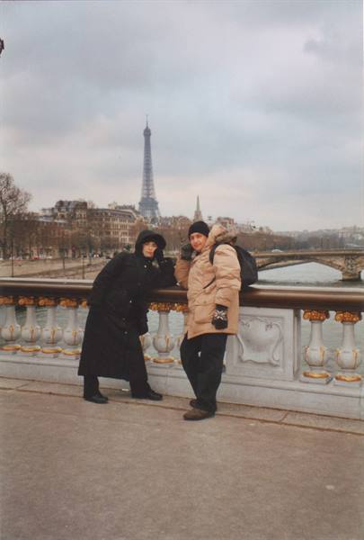 Two women pose on a stone bridge, the Eiffel Tower behind them