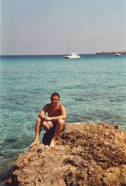 Man sitting on limestone rock, turquoise sea with anchored catamaran