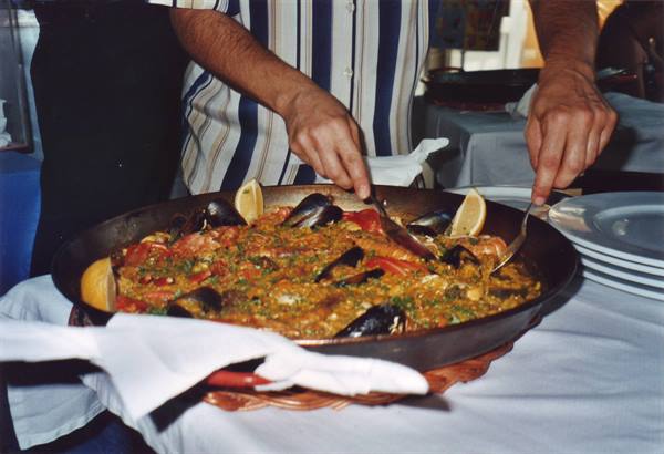 Hands serving a large seafood paella with lemon in a pan