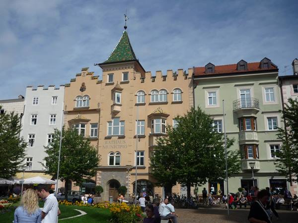 Bruneck town hall with green turret, people sitting in the square among trees