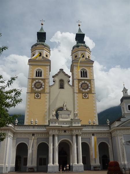 Brixen Cathedral: yellow baroque facade with twin bell towers, cloudy sky