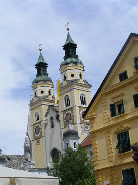The twin baroque towers of Brixen Cathedral among yellow buildings