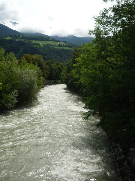 Rushing river flanked by green trees and cloud-covered mountains