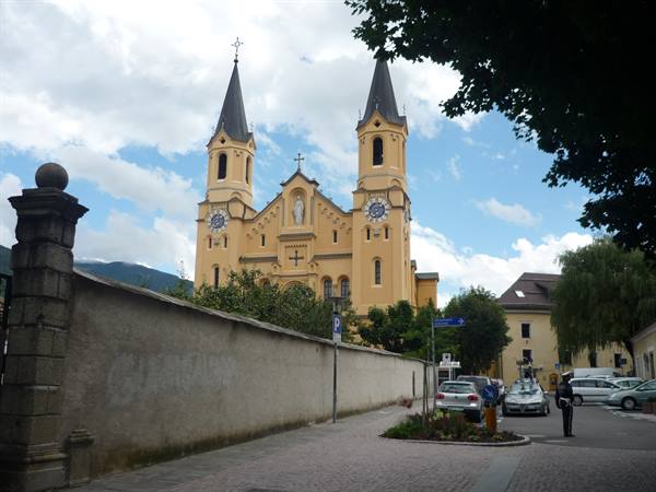 Yellow twin-towered church with clock faces beyond a stone wall