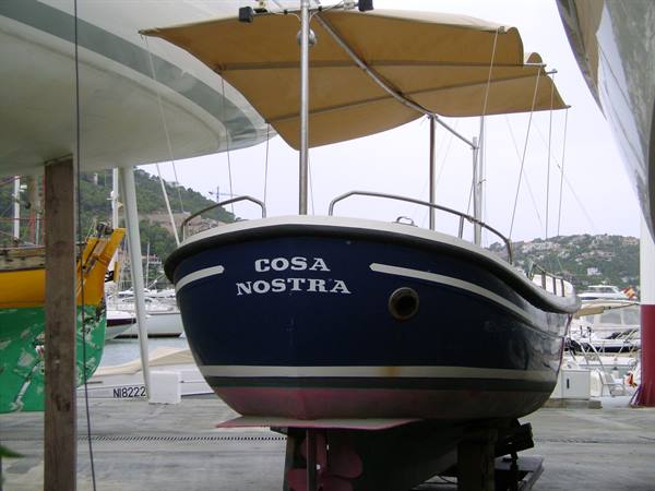 Blue boat Cosa Nostra under beige canopy, hauled up in the boatyard
