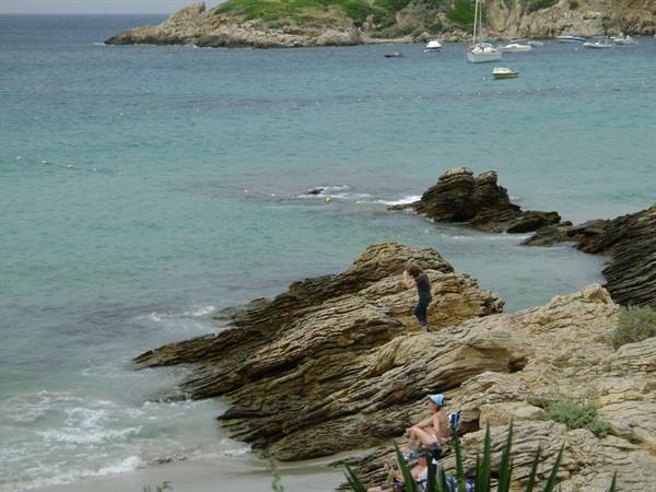 Boy standing on layered rocks, boats anchored in the turquoise bay