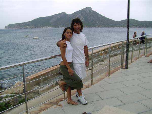 Couple in white hugging on a seaside promenade with mountains across the bay