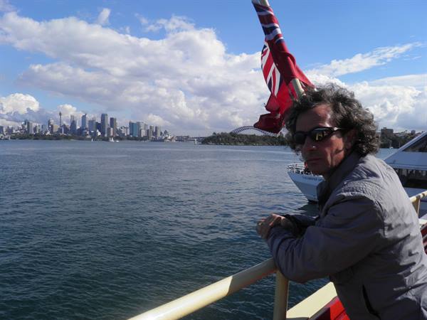 Man in sunglasses leans on ferry railing, Sydney Harbour Bridge in the background