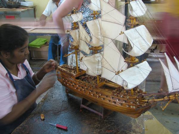 Craftswoman assembling a wooden sailing ship model with white sails in a workshop