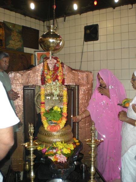 Woman in pink sari lights a flame before the flower-adorned deity in the temple