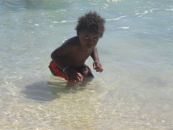 Curly-haired toddler crouching in shallow clear sea water over sand