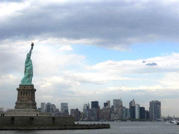 The Statue of Liberty with torch raised, Manhattan skyline behind cloudy sky