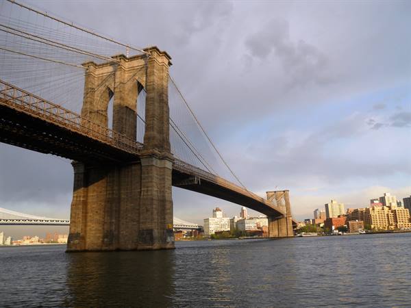 Granite towers of the Brooklyn Bridge over the East River, city skyline behind