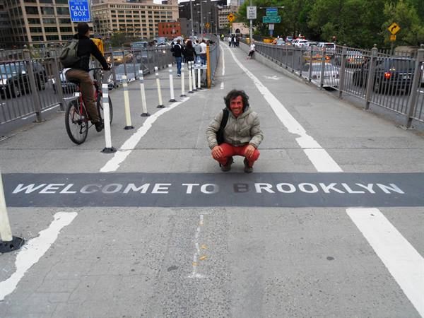 Man crouching next to the Welcome to Brooklyn marking on the bridge