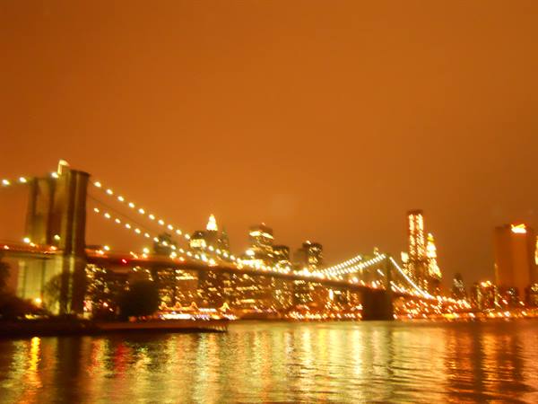 Brooklyn Bridge lit up at night, reflections on the East River