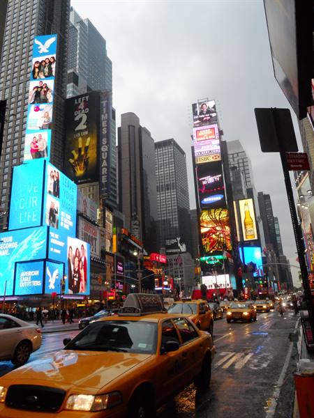 Yellow taxi beneath glowing billboards in Times Square, rain-soaked street