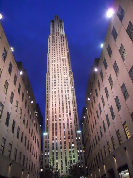 Rockefeller Center tower at night between lit buildings, dark blue sky