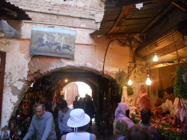 Marrakech medina alley: lit butcher stall, crowd passing under the arch