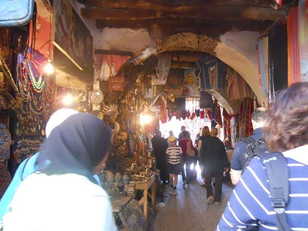 Tourists and veiled women walking through covered souk stalls of lanterns and crafts