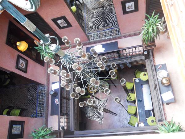 Metal chandelier seen from above inside a pink riad with zebra rugs and green chairs