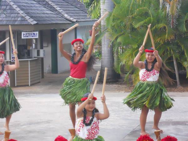 Hula dancers in green leaf skirts with black flower leis performing
