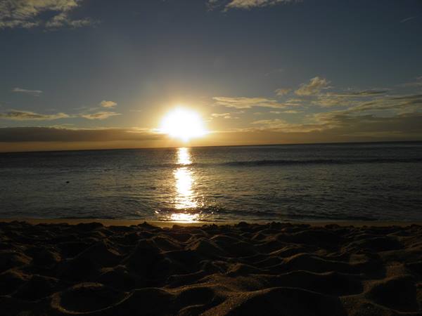 Low sun over the ocean reflecting on water, shaded sand in foreground